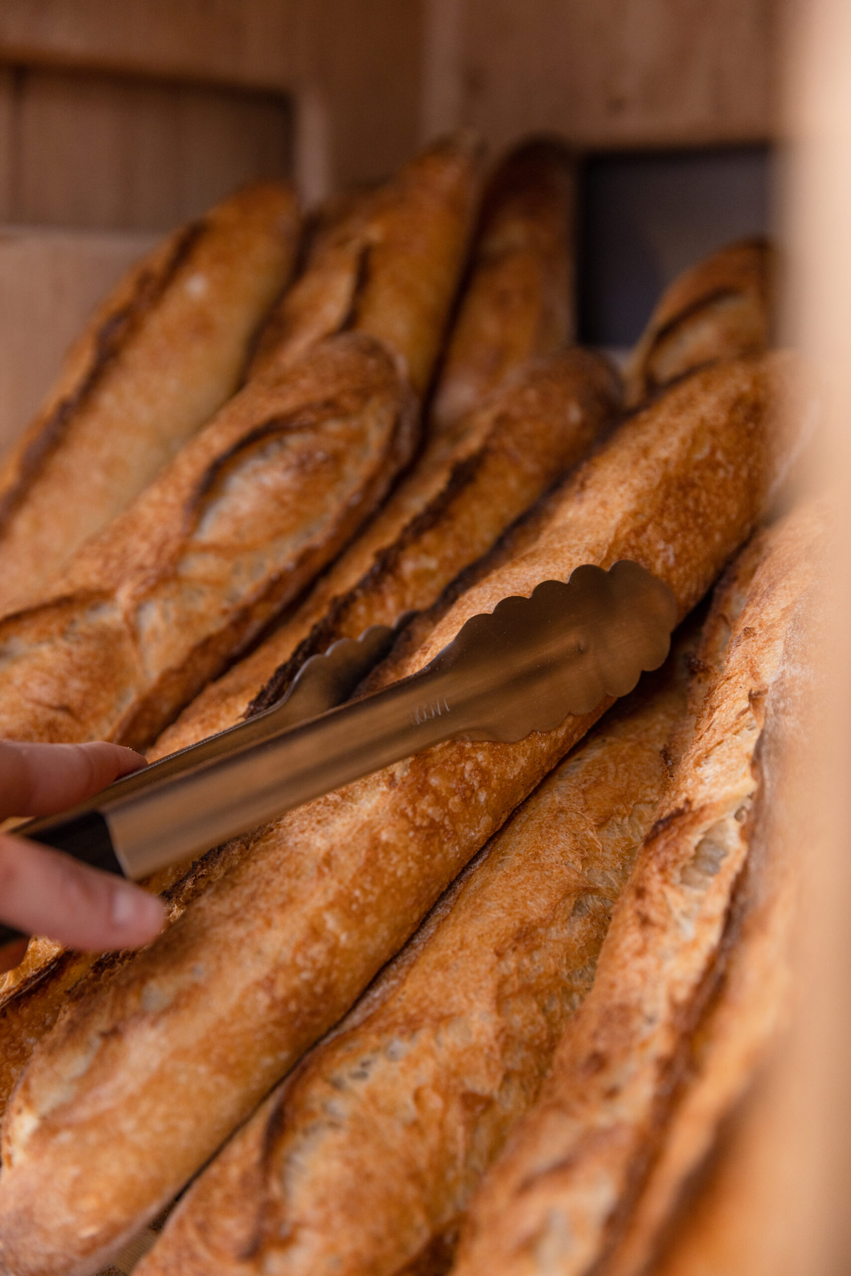 Une baguette de tradition française est attrapée avec une pince par un boulanger.