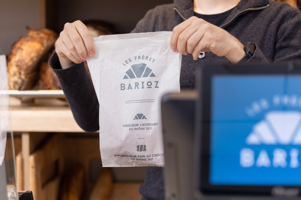 Un vendeur s'apprête à remettre un produit emballé dans un sachet à un client de la boulangerie des Frères Barioz.