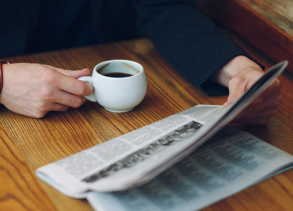 Man's hands close-up holding cup of coffee and a newspaper